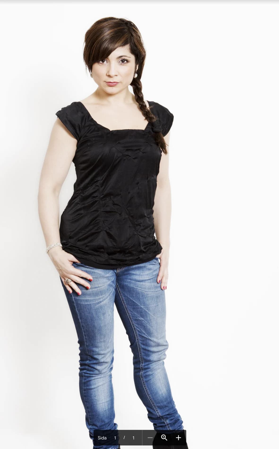 Ayla Kabaca i svart topp och jeans står med tummarna i fickorna och flätan över axeln mot vit bakgrund