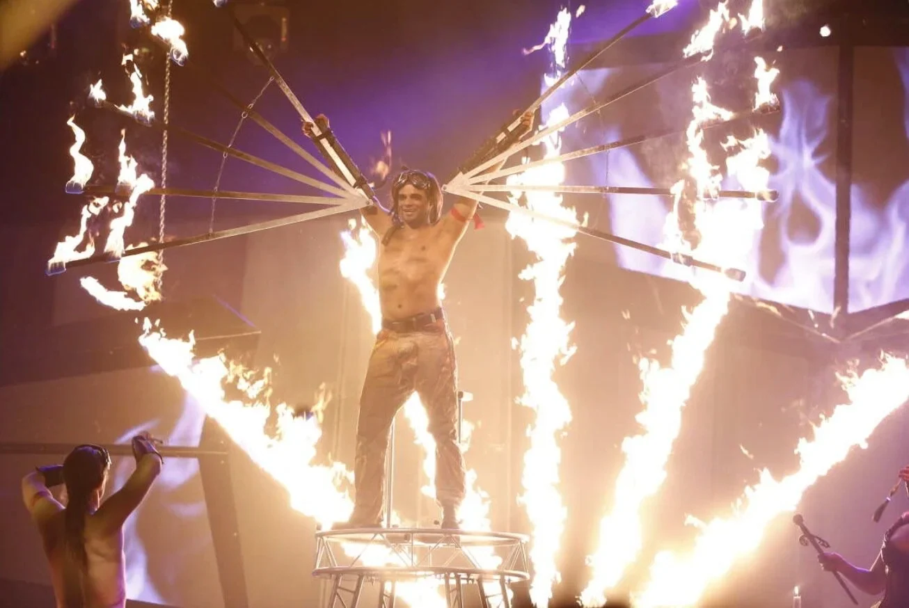 David Hammarberg står på en ställning och breder ut brinnande eldvingar under en show