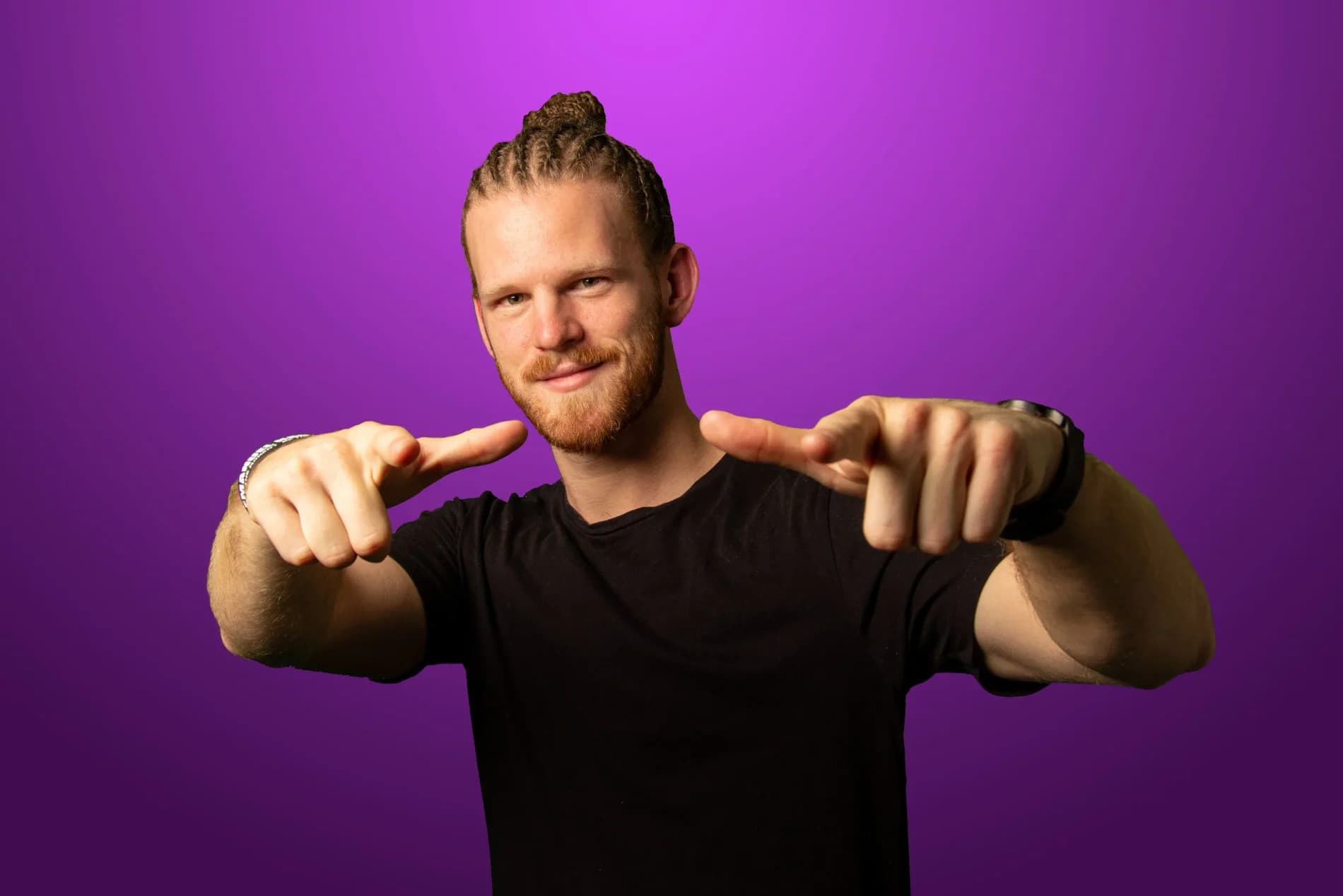 Emanuel Hansson pekar med båda pekfingrarna mot kameran, i svart t-shirt mot lila bakgrund