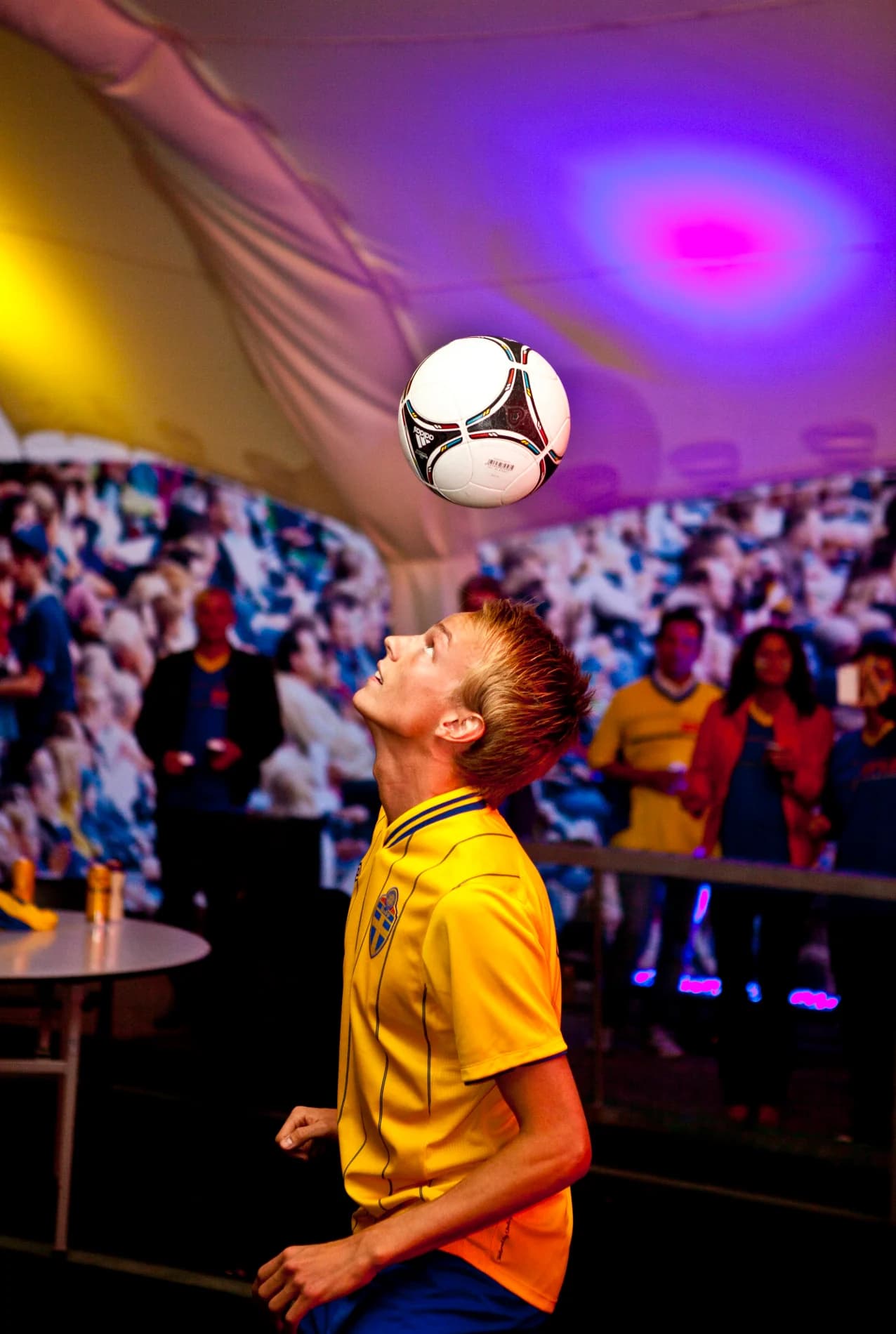 Emil Jylhänlahti i gul landslagströja balanserar en fotboll ovanför pannan inne i ett festtält