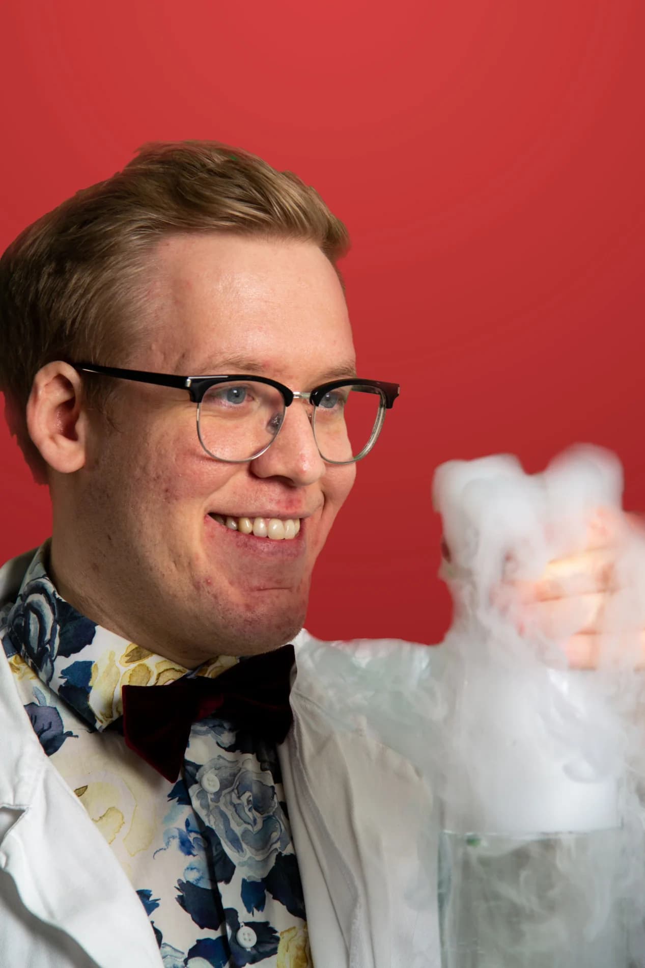 Freddy Grip ler och håller upp en rykande bägare med vit dimma mot röd bakgrund