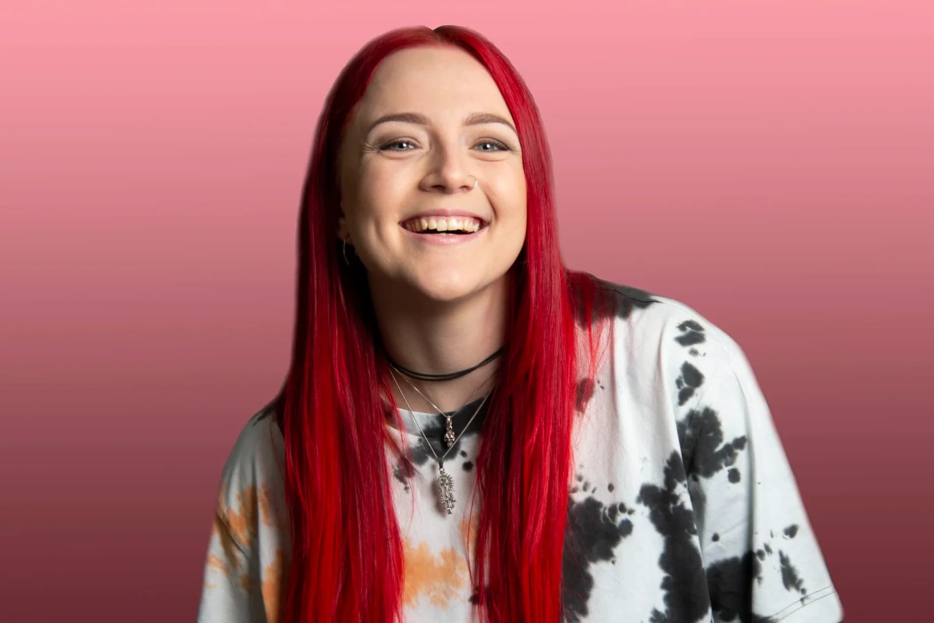 Linnéa Elfström Schederin med långt rött hår skrattar i batikmönstrad t-shirt mot rosa bakgrund