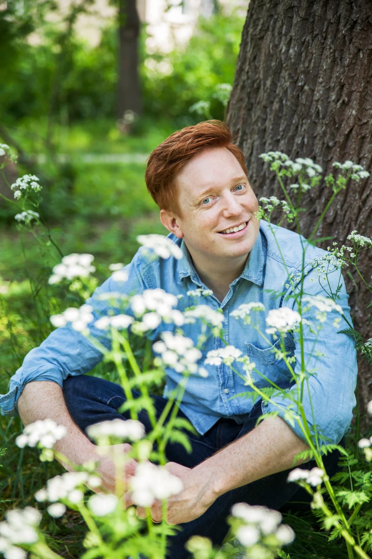 Markus Granseth sitter i grönskan bland vita hundkäxblommor vid en trädstam