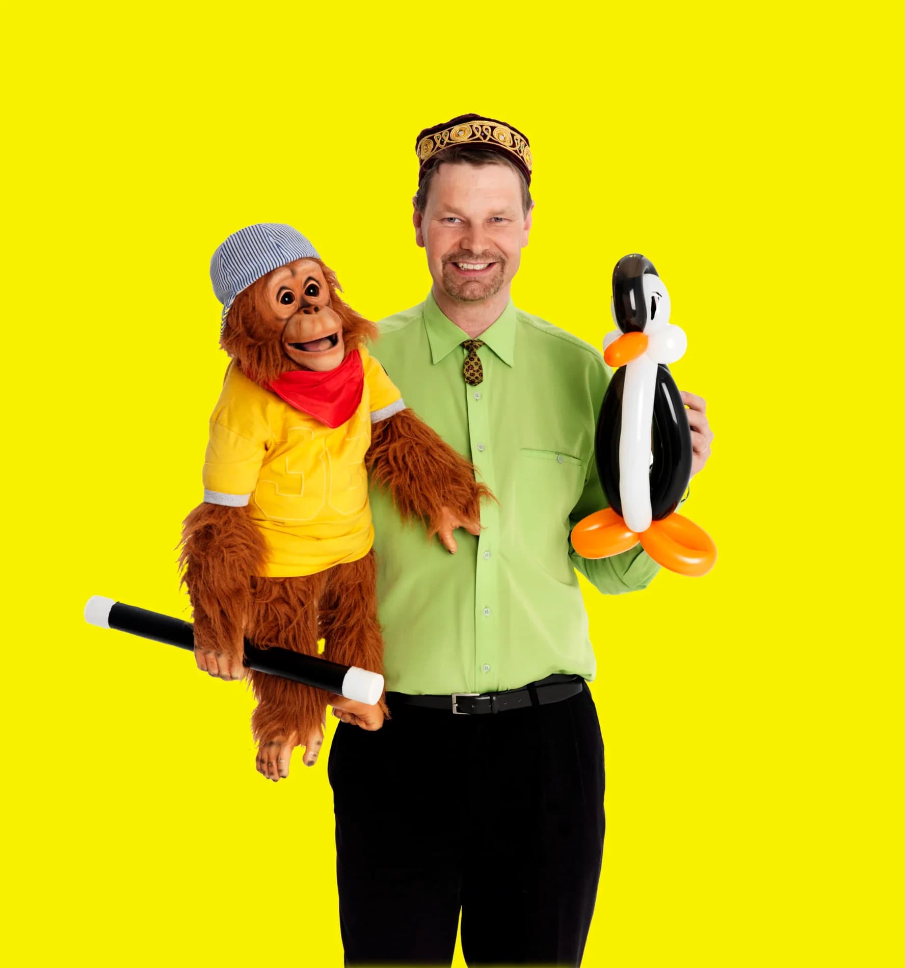 Mr. Goran med orangutangdocka på armen och en ballongpingvin i handen mot gul bakgrund