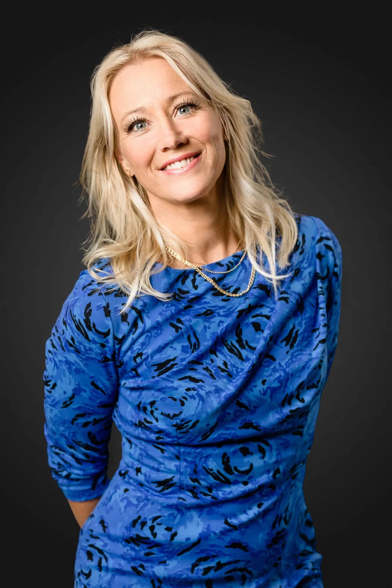 Sara Edwardsson lutar huvudet åt sidan och ler i blåmönstrad klänning, händerna bakom ryggen