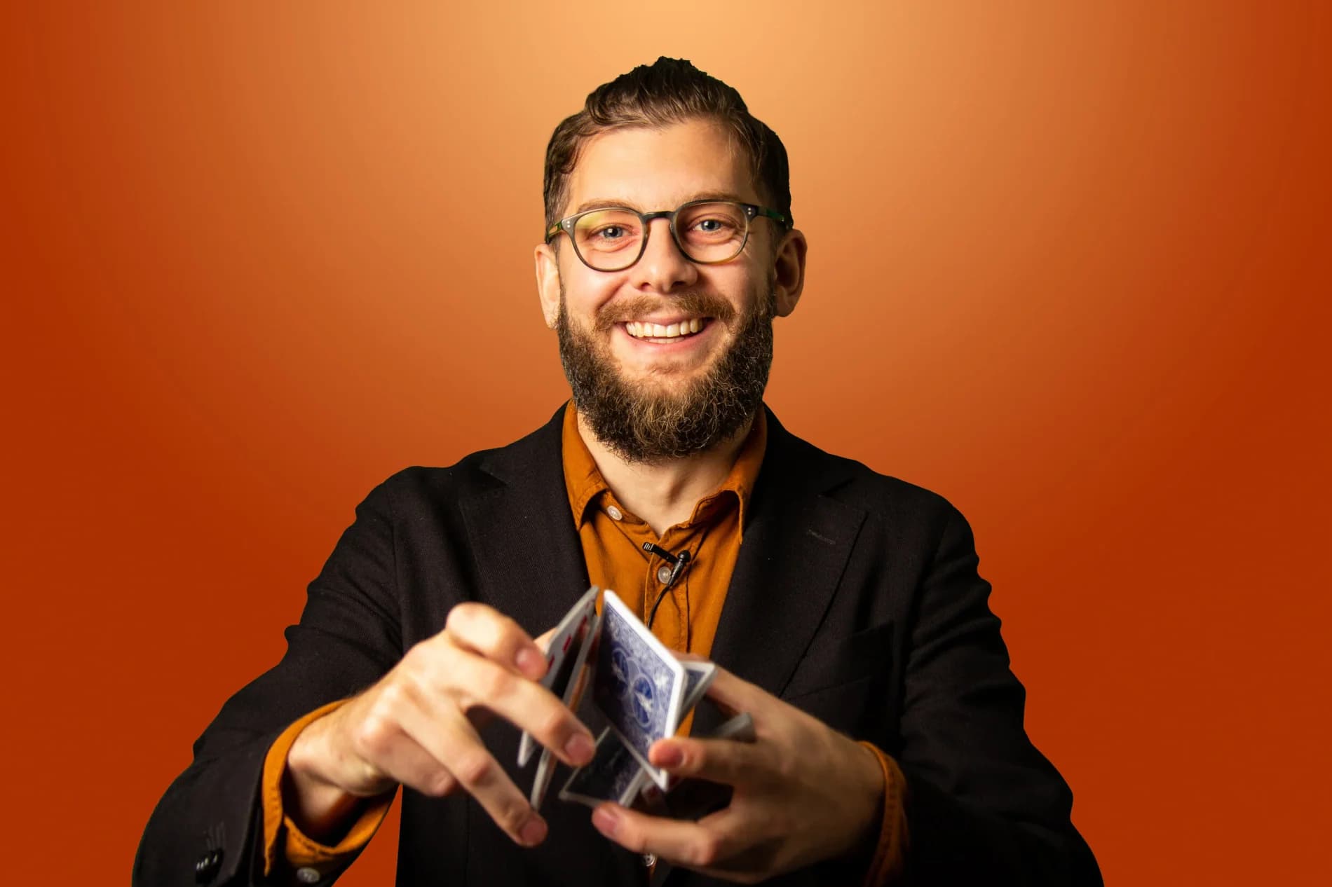 Simon Söderqvist låter en kortlek kaskadera mellan händerna framför orange fond